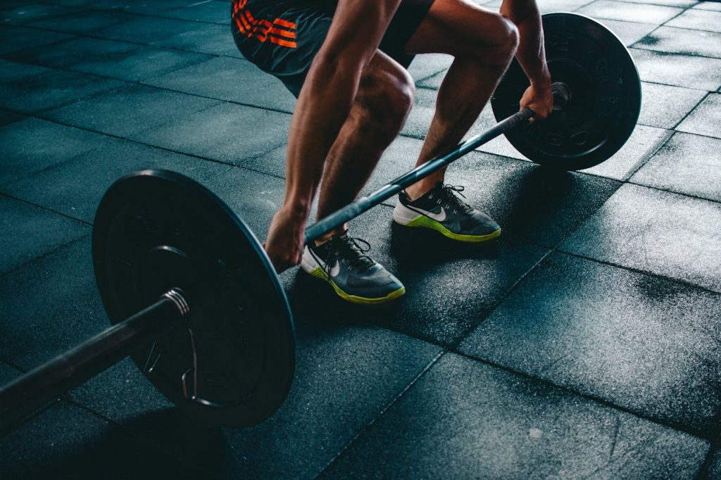 person-holding-barbell-841130 Man performing a deadlift exercise in a gym, demonstrating strength and fitness.